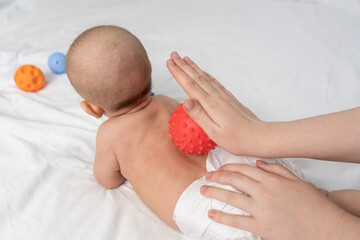 Doctor hands massage newborn with red rubber ball