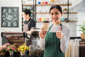 Happy beautiful asian young barista woman in apron holding cup coffee with serving to customer in cafe.