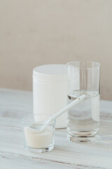 Collagen powder in bowl, glass of water and measure spoon on a white wooden background. Extra protein intake. Natural beauty and health supplement concept.