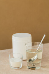 Glass with collagen dissolved in water and collagen protein powder on a light beige table. Healthy lifestyle concept.