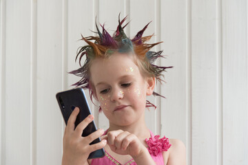A child with a beautiful hairstyle looks disappointed at the smartphone screen. The concept of frustration and bad mood. A girl with an evening hairstyle in a smart dress