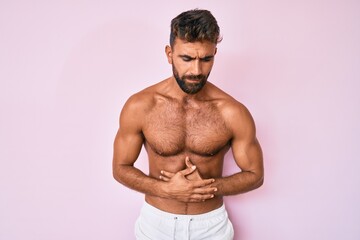 Fototapeta premium Young hispanic man standing shirtless with hand on stomach because indigestion, painful illness feeling unwell. ache concept.