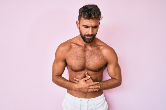 Young hispanic man standing shirtless with hand on stomach because indigestion, painful illness feeling unwell. ache concept.
