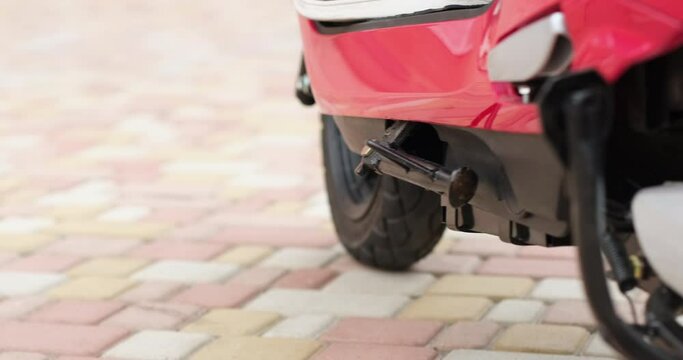 A person raises the parking step of the moped with his foot to start driving. Parking a moped on the street. Close-up from below.