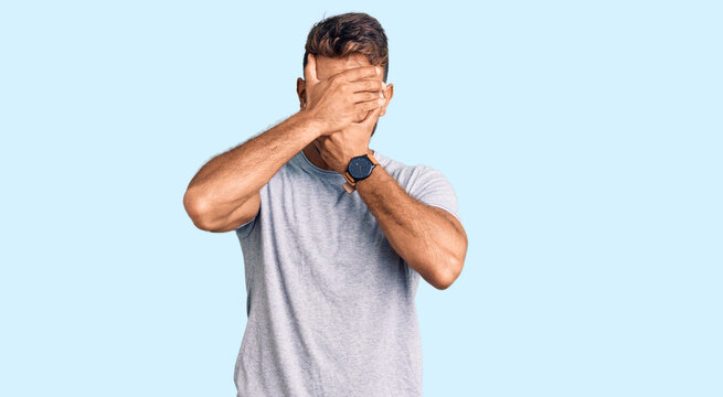 Young hispanic man wearing casual clothes covering eyes and mouth with hands, surprised and shocked. hiding emotion