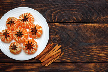 Tangerines in a white plate with star anise and cinnamon on a brown wooden background  with an empty space for text, the concept of Christmas, ingredients for warming seasonal drinks and mulled wine