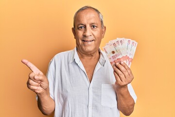Handsome mature man holding 10 colombian pesos banknotes smiling happy pointing with hand and...