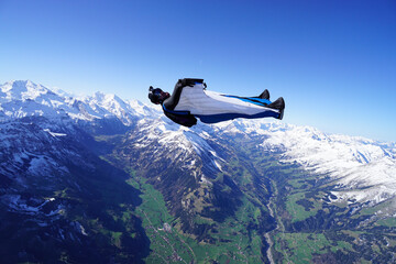 Wingsuit flier glides on his back over snowcapped mountains