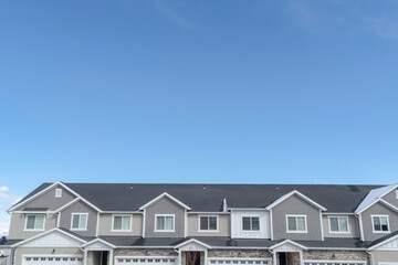 Upper storey of suburban homes with gray roofs and dormers against blue sky