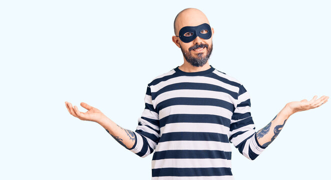 Young handsome man wearing burglar mask smiling showing both hands open palms, presenting and advertising comparison and balance