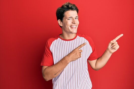 Handsome caucasian man wearing baseball uniform smiling and looking at the camera pointing with two hands and fingers to the side.