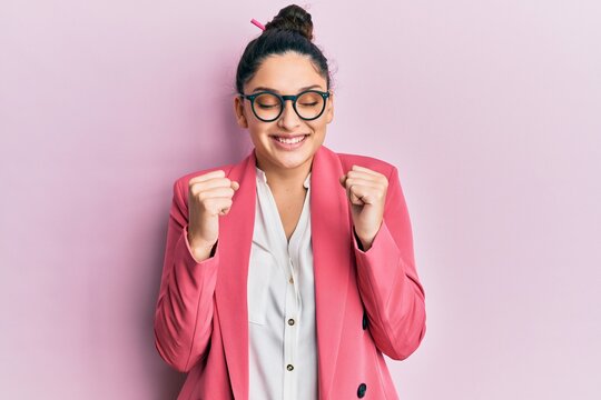Beautiful middle eastern woman wearing business jacket and glasses excited for success with arms raised and eyes closed celebrating victory smiling. winner concept.