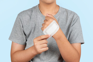 Boy putting adhesive bandage, plaster or band-aid on a cut hand isolated on blue background....