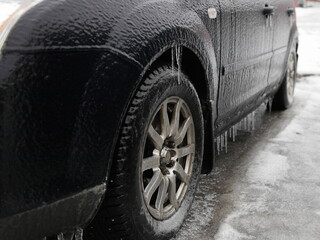Ice-covered car side view in perspective, wheel and icicles on threshold, icy vehicle on a winter...