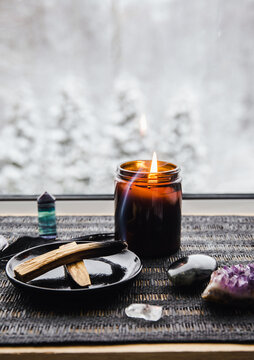 Palo Santo wood known as oily aromatic holy wood sticks smouldering on plate on home window sill cleaning negative energy concept. Beautiful winter landscape on background blurred with copy space.