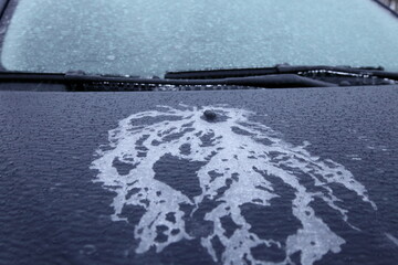 Beautiful ice pattern on the bonnet of the car, non-freezing washer fluid from washing nozzle under the ice on the hood cover on icy windglass and wipers background after freezing rain at winter day