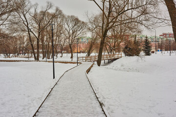Winter park landscape.The city park is covered with snow. Snow on the wooden sidewalks and bridges of the park is trampled by the walking. The bridges are fenced with wooden railings. 