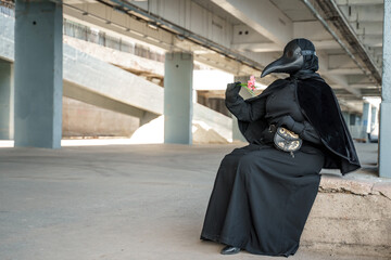 plague doctor in an empty city on an empty marina holds a flower