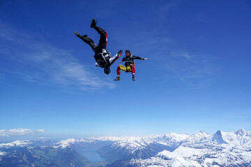 Naklejka na ściany i meble Skydivers perform tricks above snowcapped mountains
