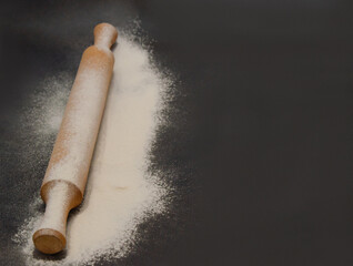 Rolling pin and white flour on a dark background. Cooking