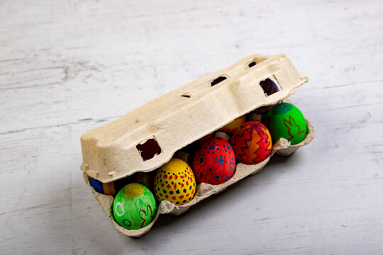 Painted Eggs With Easter Motives In A Closed Egg Carton On A Wooden Board