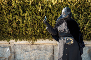 plague doctor holds a vaccine against a background of plants