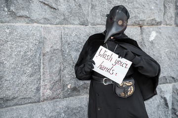 plague doctor holds a sign saying wash your hands