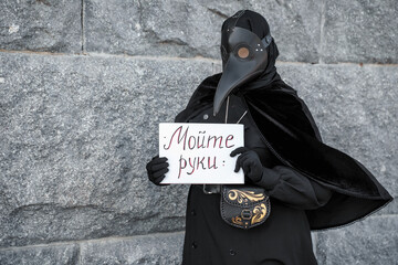 plague doctor holds a sign saying wash your hands