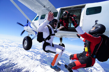 Skydivers jump out of plane and perform tricks above snowcapped mountains