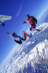 Skydivers jump out of plane and perform tricks above snowcapped mountains
