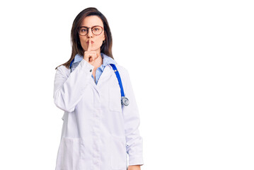 Young beautiful woman wearing doctor stethoscope and glasses asking to be quiet with finger on...