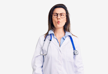 Fototapeta premium Young beautiful woman wearing doctor stethoscope and glasses making fish face with lips, crazy and comical gesture. funny expression.