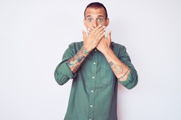 Young handsome man with tattoo wearing casual clothes shocked covering mouth with hands for mistake. secret concept.