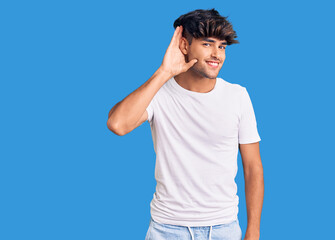 Young hispanic man wearing casual clothes smiling with hand over ear listening an hearing to rumor or gossip. deafness concept.