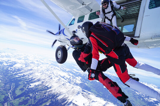 Skydivers jump out of airplane above snowcapped mountains