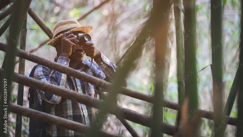 Wall mural African man photographer holding camera with backpack standing in the green natural background