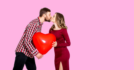Girl and guy kiss on a pink background and hold in their hands a large inflatable red ball in the shape of a heart. Concept of the holiday - Valentine's Day, International Women's Day, Mother's Day.