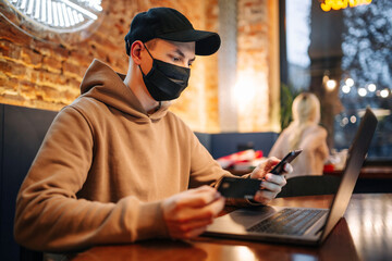 Shopping and online payment using cellphone, laptop and credit card. Man wearing black medical mask...