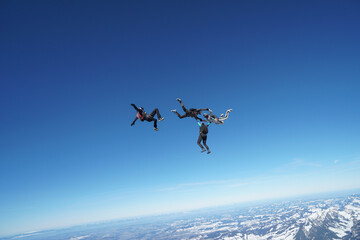Fototapeta na wymiar Skydivers perform stunts above snowcapped mountains