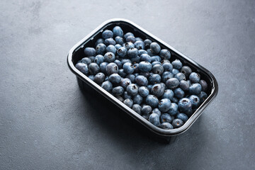 Organic blueberries in black plastic container or box on black concrete background