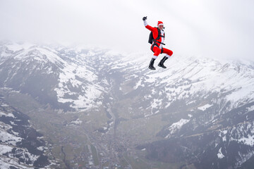 Fototapeta na wymiar Skydiver dressed in Santa Claus outfit flies above snowcapped mountains