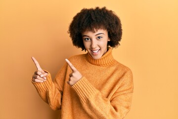 Young hispanic girl wearing wool winter sweater smiling and looking at the camera pointing with two hands and fingers to the side.