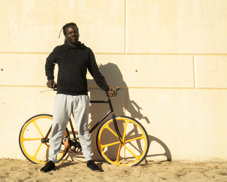 Afro man with dreadlocks with an urban bicycle on a city wall. Concept: sustainable mobility