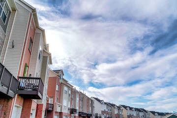 Bright sun in the cloudy blue sky over three storey townhouses in the valley