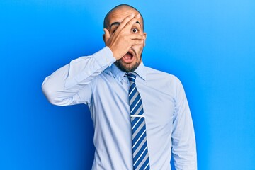 Hispanic adult man wearing business shirt and tie peeking in shock covering face and eyes with hand, looking through fingers afraid