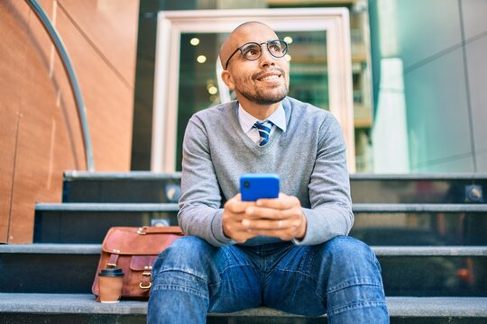 Young african american businessman smiling happy using smartphone sitting on the stairs at the city.