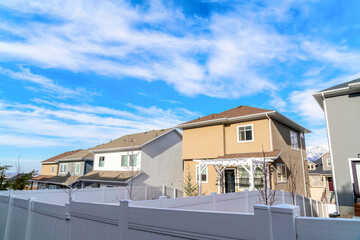 Two storey homes with white wooden fences beneath bright clouds and blue sky