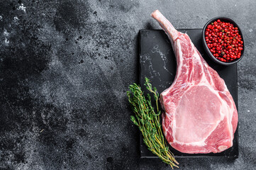 Raw fresh tomahawk pork chop steak on a marble board. Black background. Top view. Copy space