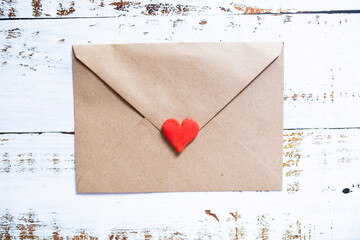 Love letter in a craft envelope with clay red heart on white wood background.