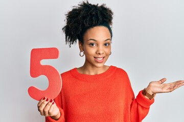 Young african american girl holding number five celebrating achievement with happy smile and winner expression with raised hand